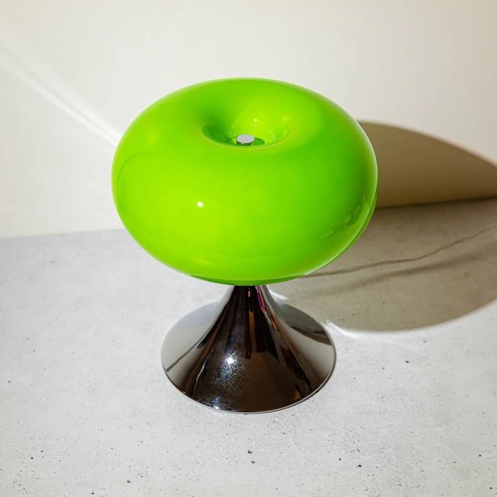 Space age table lamp in green showing rounded glass sphere on a concrete floor.