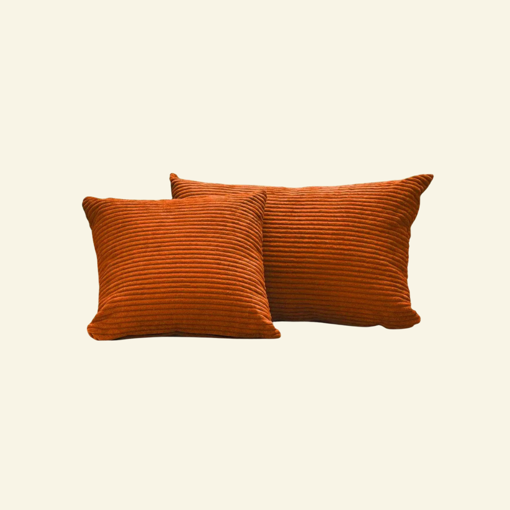 Two orange textured corduroy pillows on a beige background