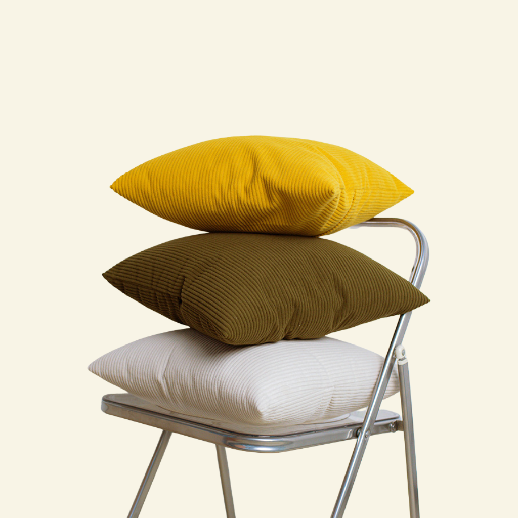 Chair with three stacked corduroy cushions in yellow, brown, and white on a light beige background