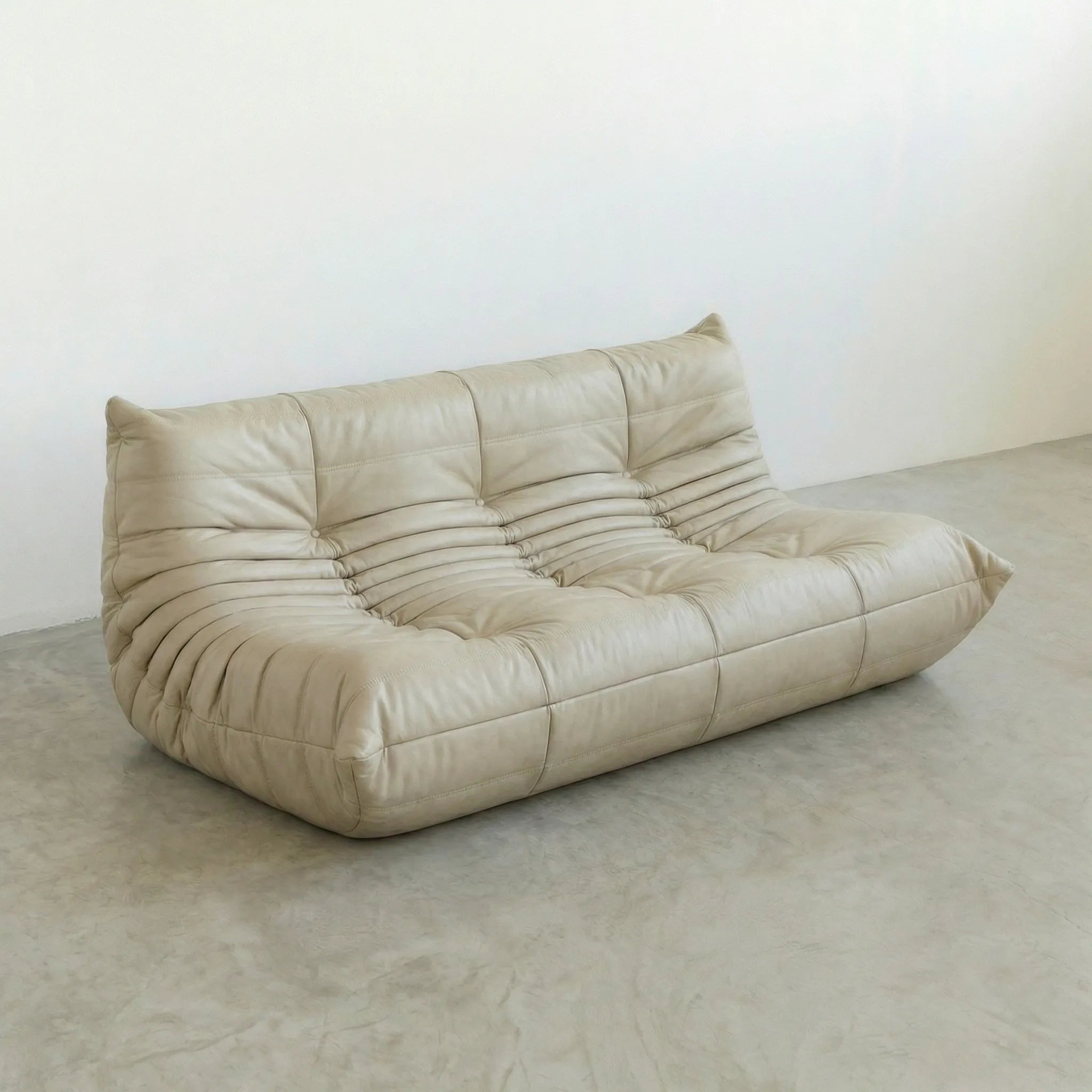 Beige leather 3-seater togo sofa dupe on a gray floor with a white wall background