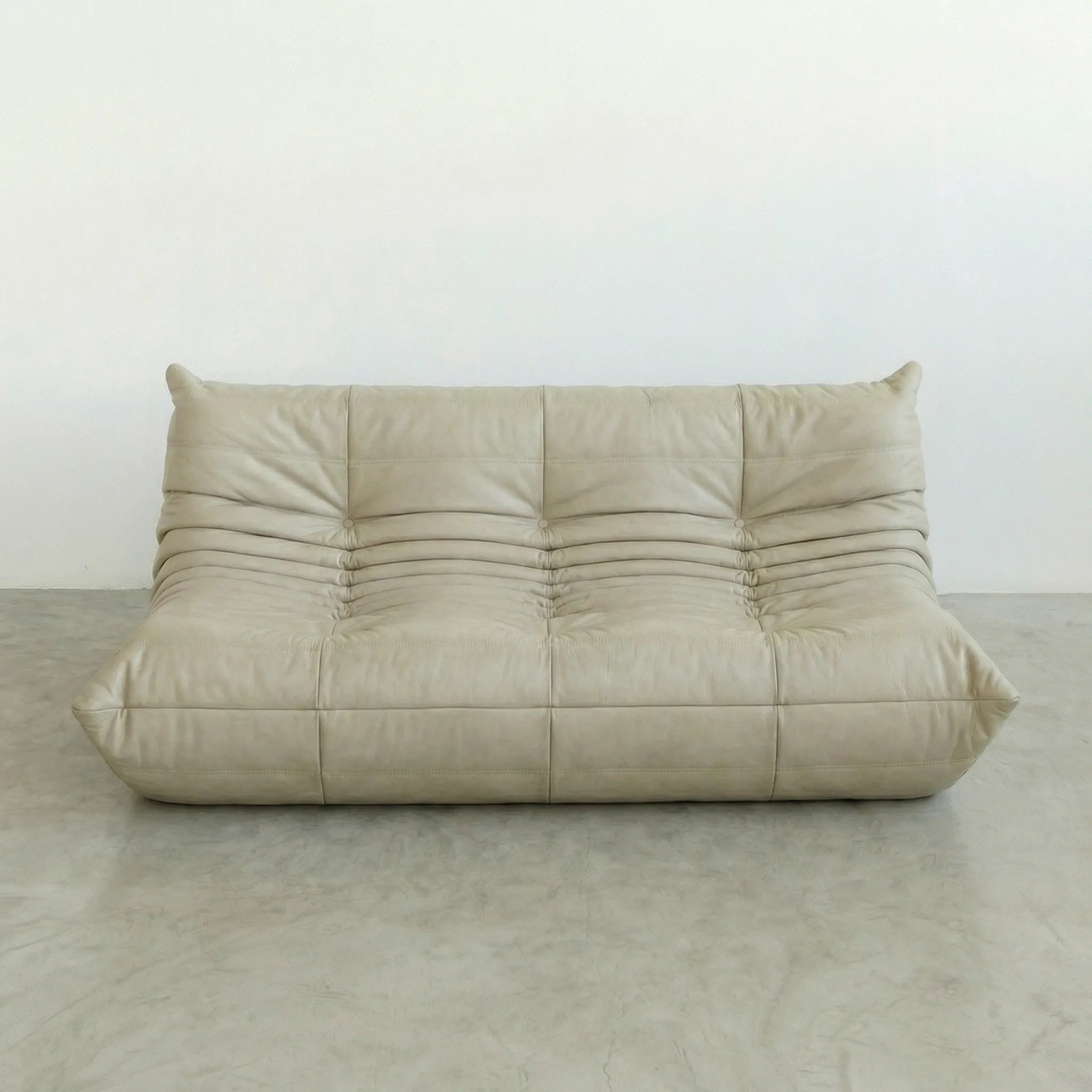 Beige leather 3-seater togo sofa dupe on a gray floor with a white wall background