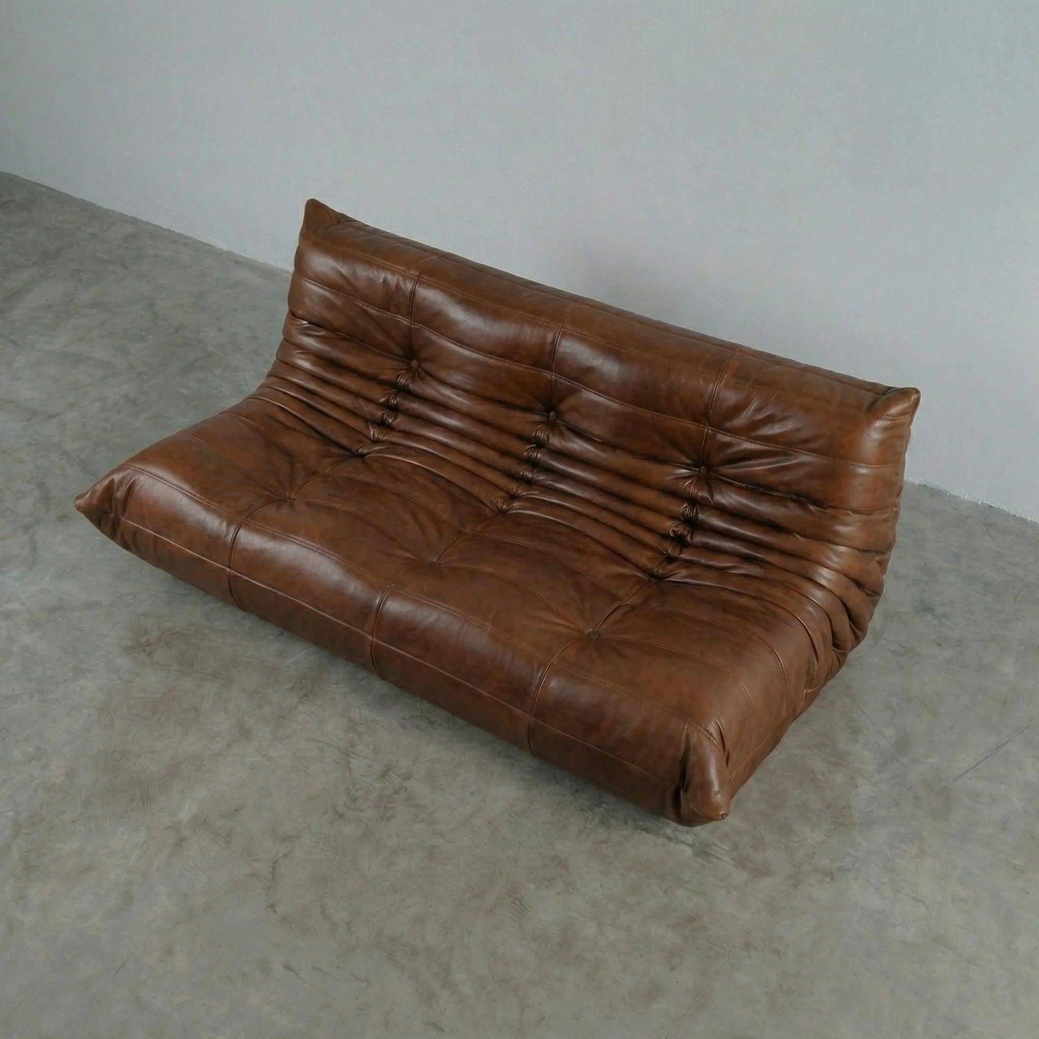 Brown leather 3-seater sofa dupe on a gray floor with a plain white wall background
