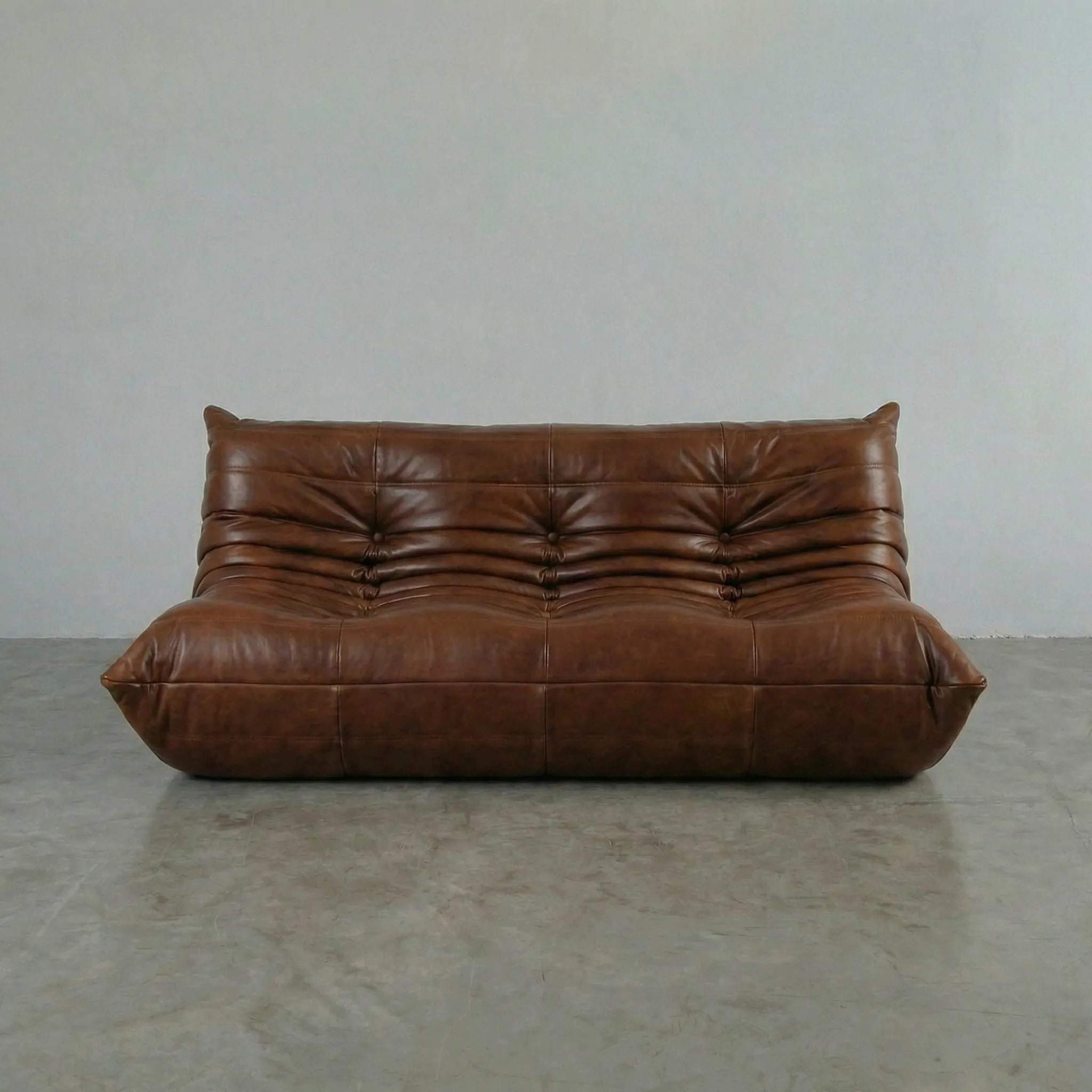Brown leather 3-seater sofa dupe on a gray floor with a plain white wall background