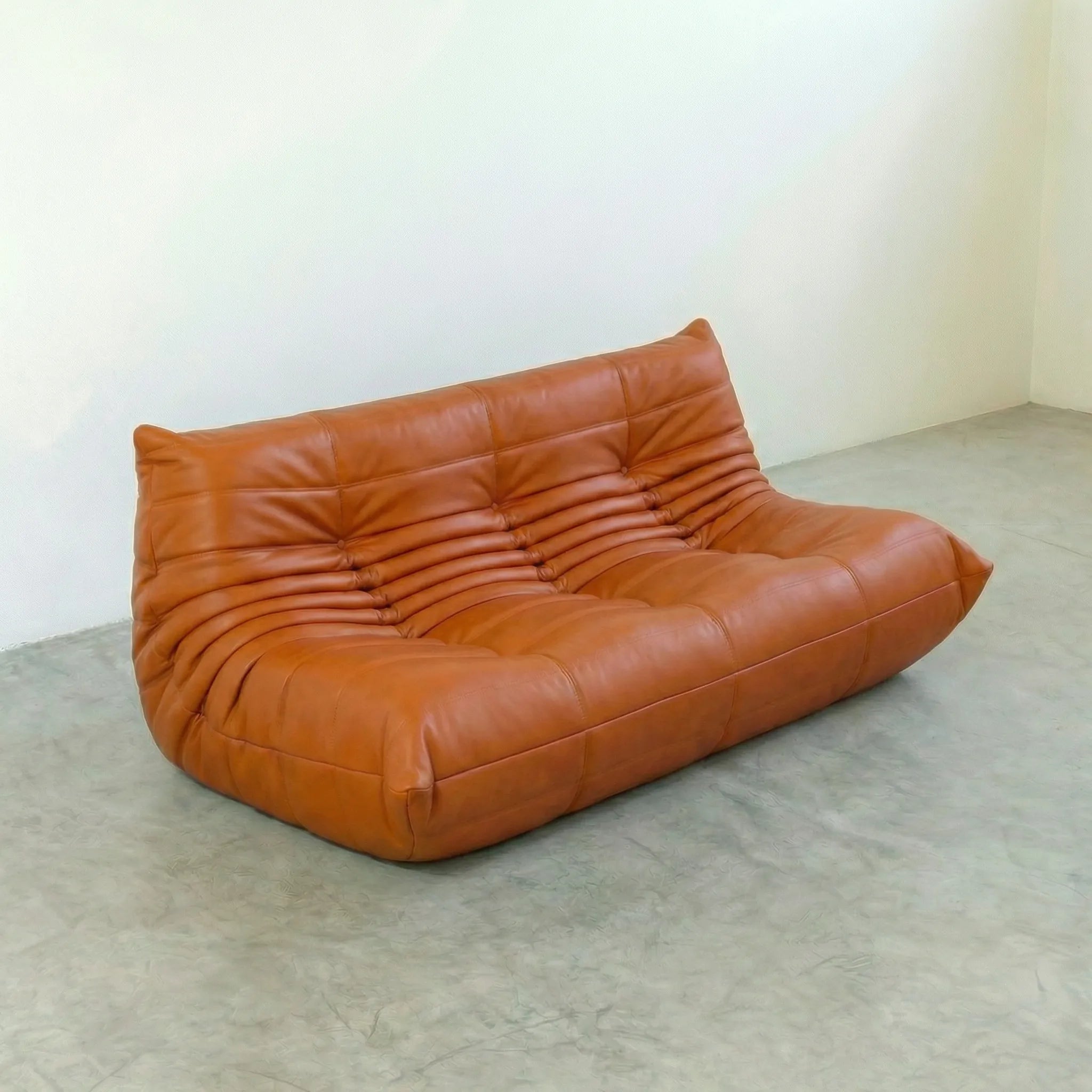 Cognac leather 3-seater sofa dupe in a minimalistic room with white walls and gray floor.