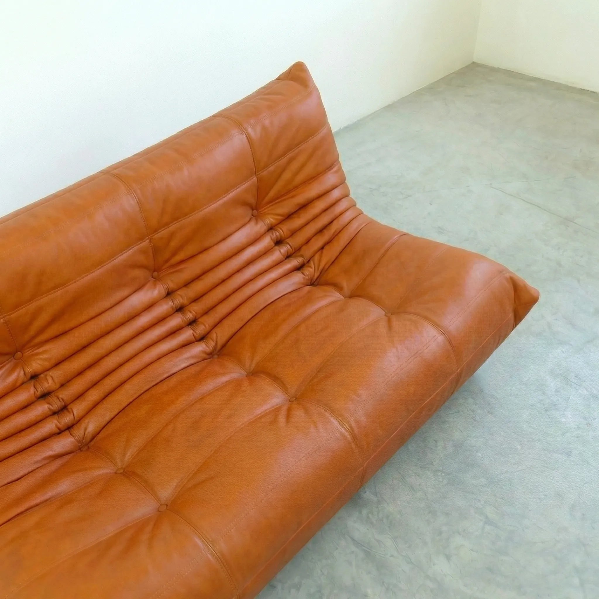 Cognac leather 3-seater sofa dupe in a minimalistic room with white walls and gray floor.