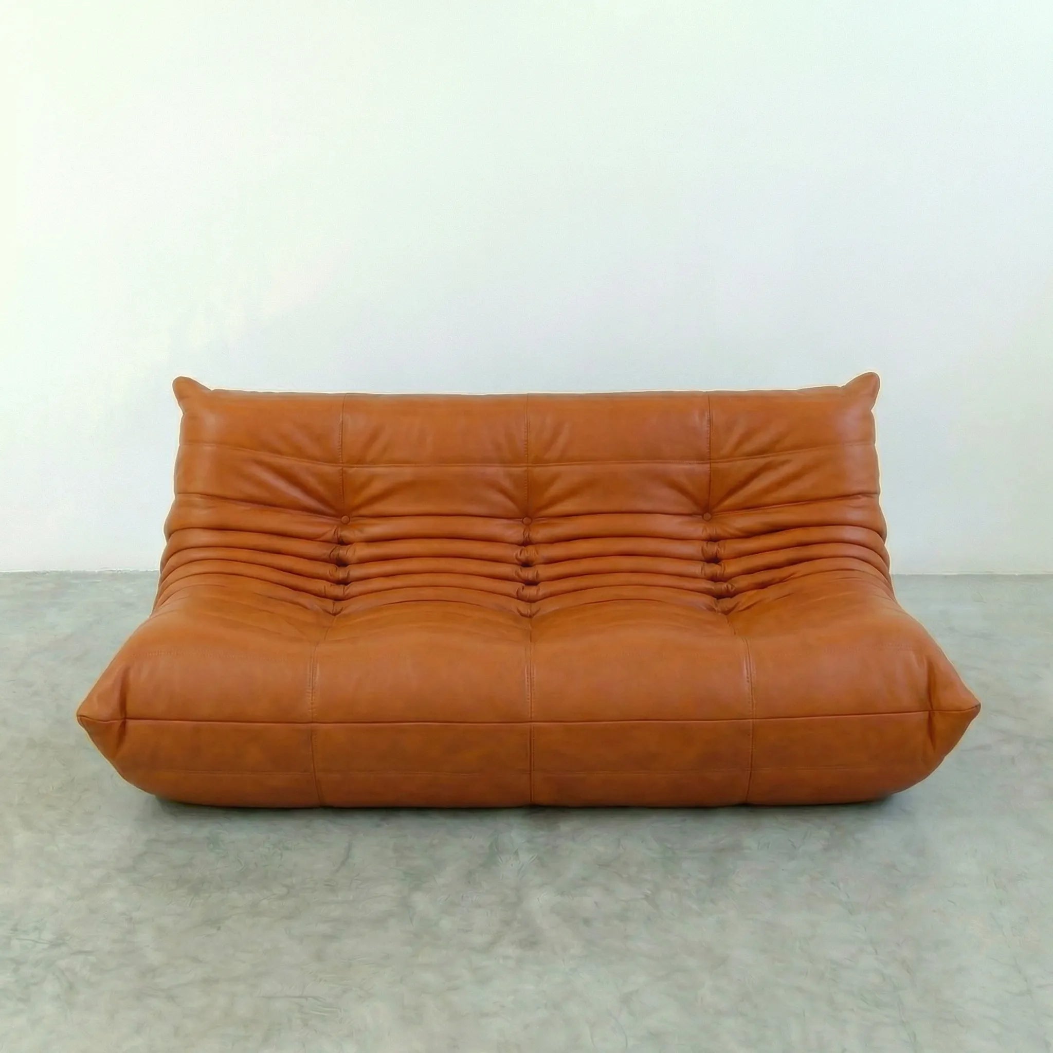 Cognac leather 3-seater sofa dupe in a minimalistic room with white walls and gray floor.