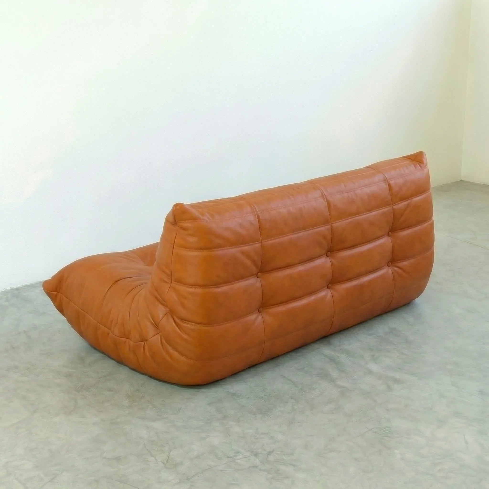 Cognac leather 3-seater sofa dupe in a minimalistic room with white walls and gray floor.