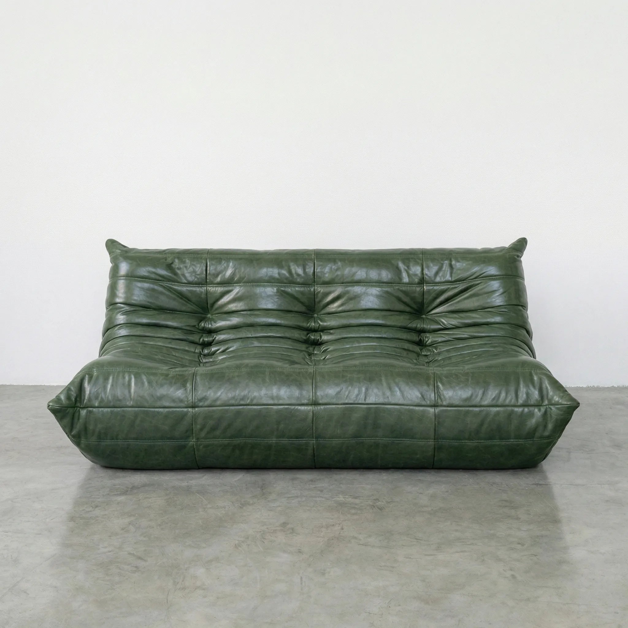 Green leather togo sofa dupe on a concrete floor with a white wall background