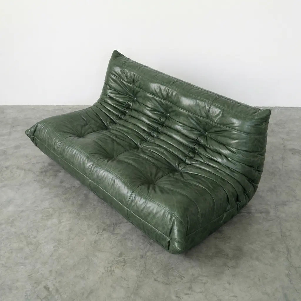 Green leather togo sofa dupe on a concrete floor with a white wall background