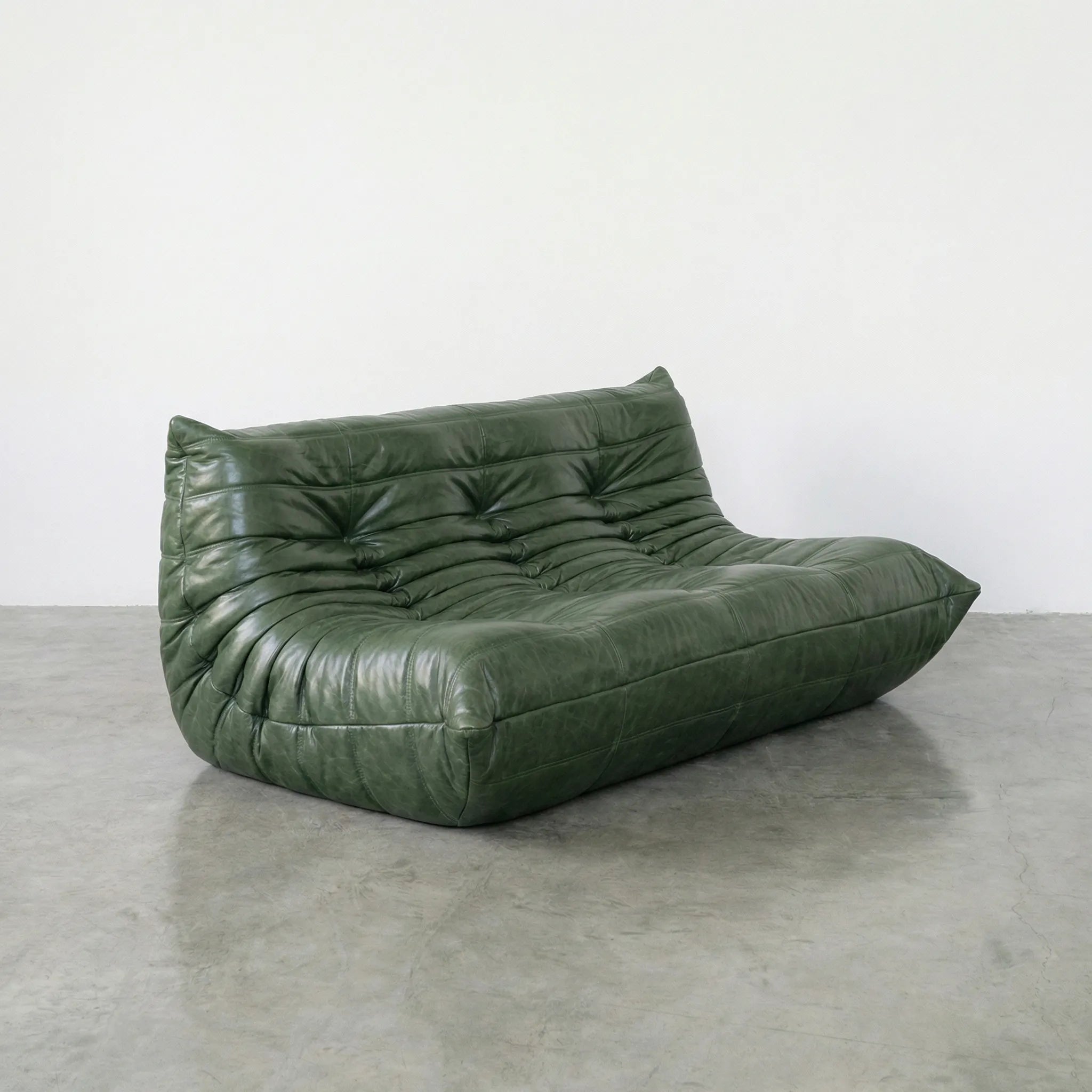Green leather togo sofa dupe on a concrete floor with a white wall background