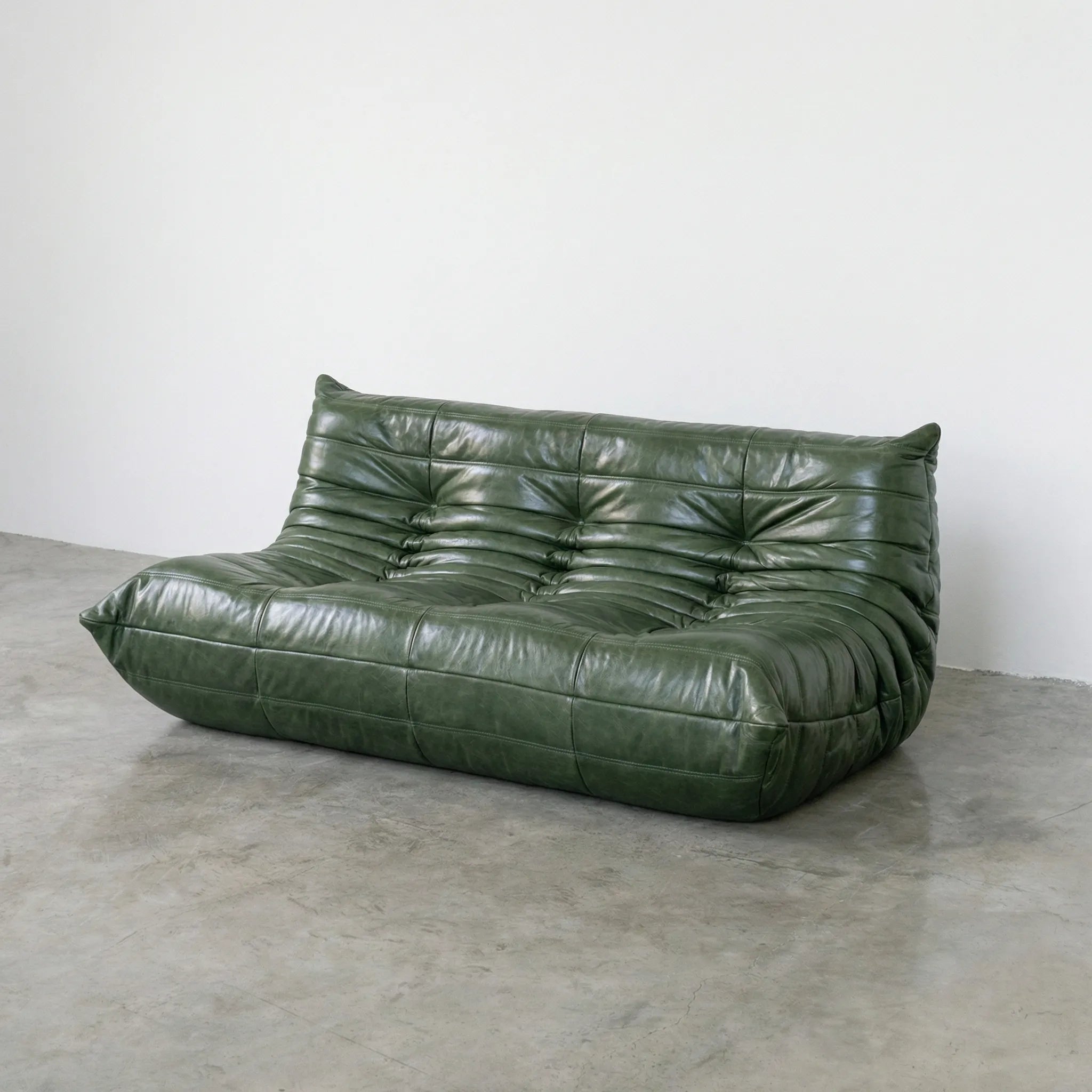 Green leather togo sofa dupe on a concrete floor with a white wall background