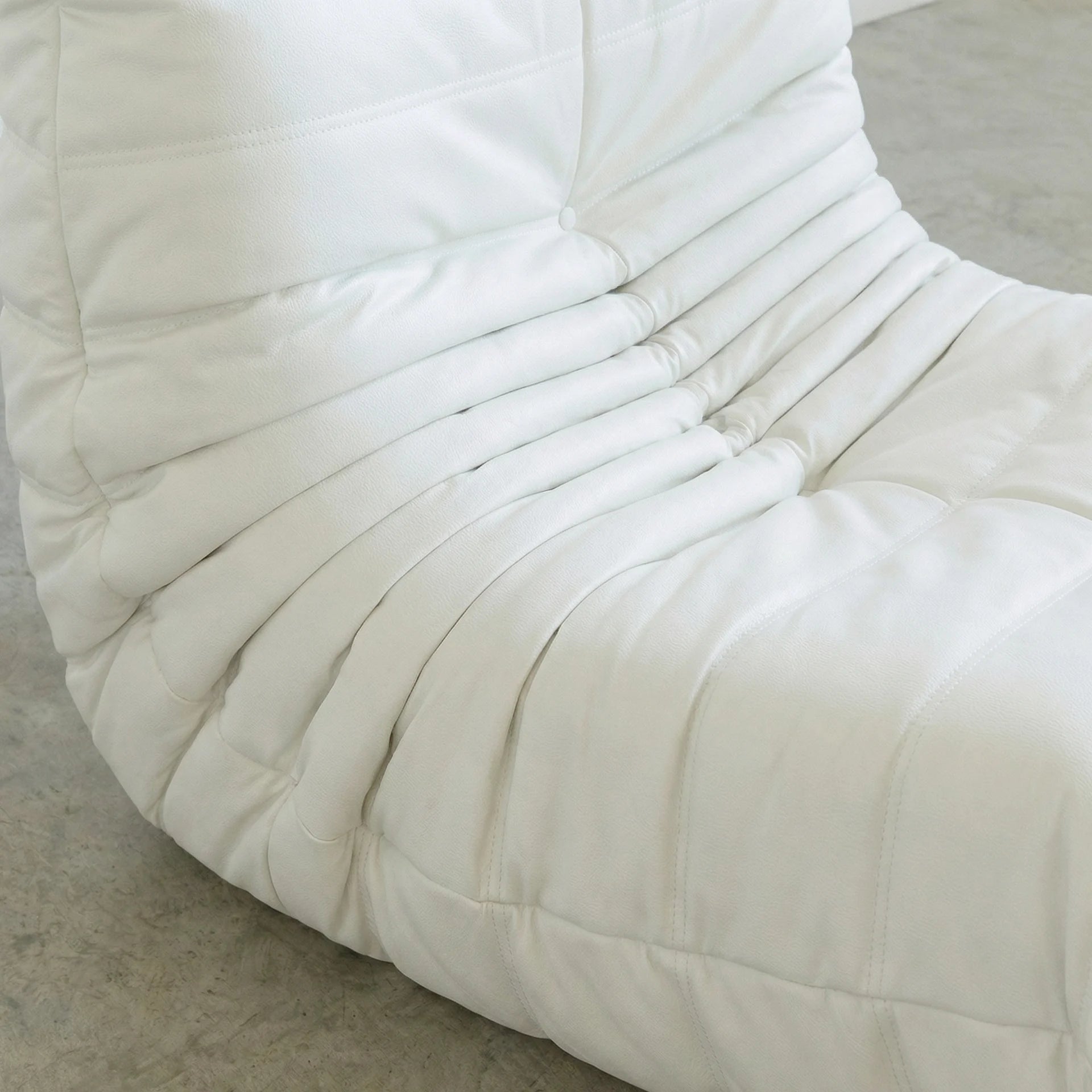 Close up of the Togo Chair Dupe in white faux leather on a concrete floor with a white wall background