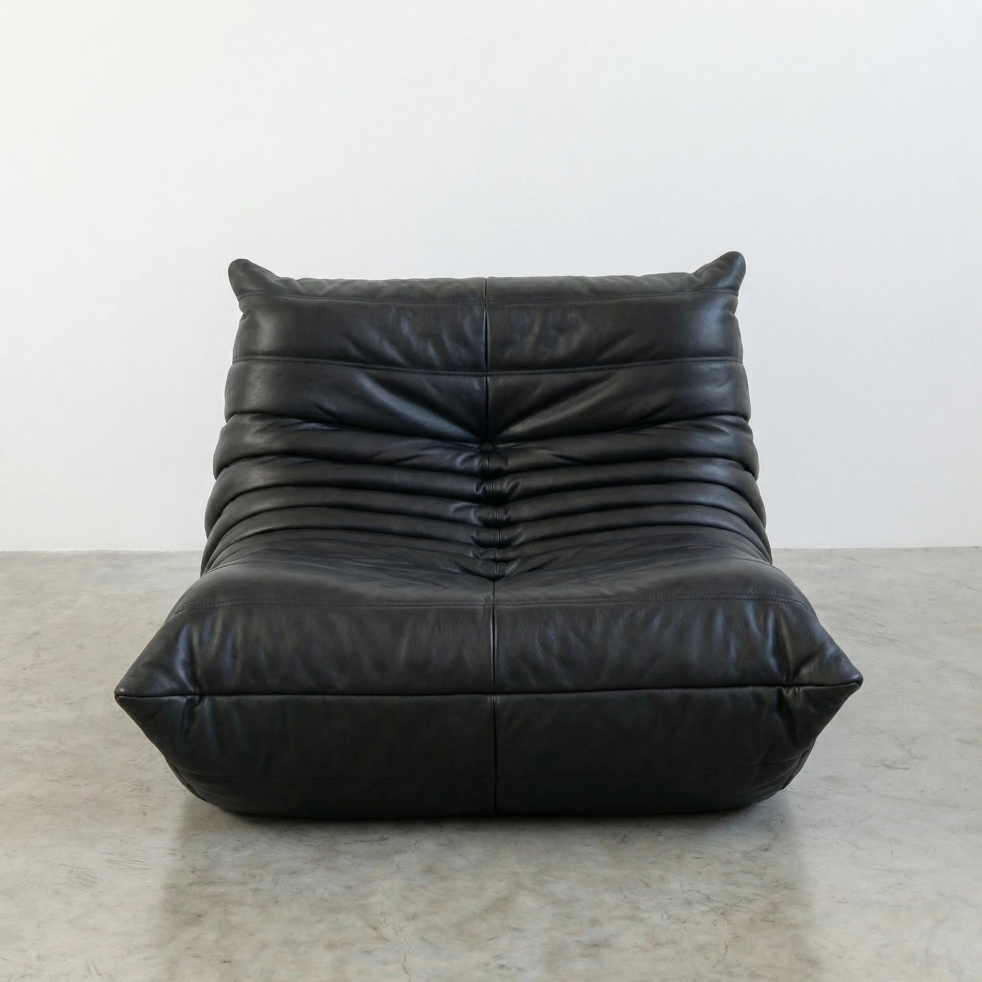 Togo Chair Dupe in black real cowhide leather on a concrete floor with a white wall background