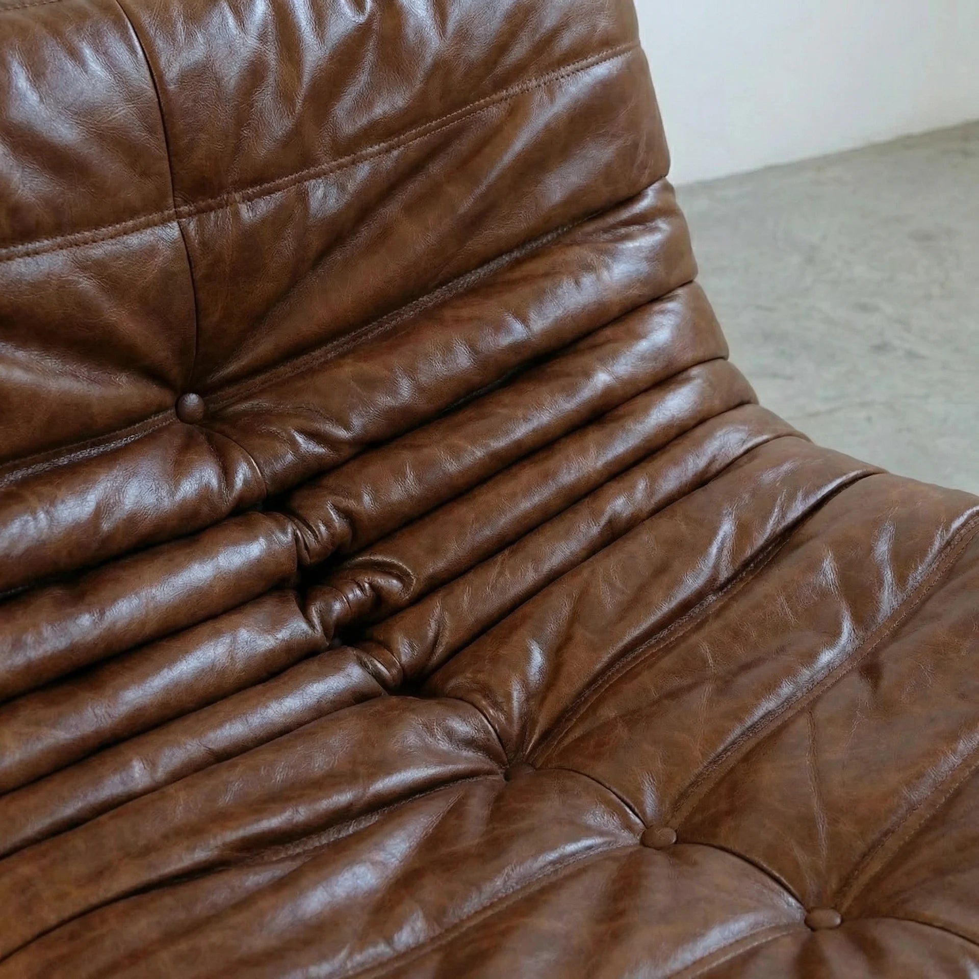 Close-up of a brown togo sofa dupe in leather with visible stitching