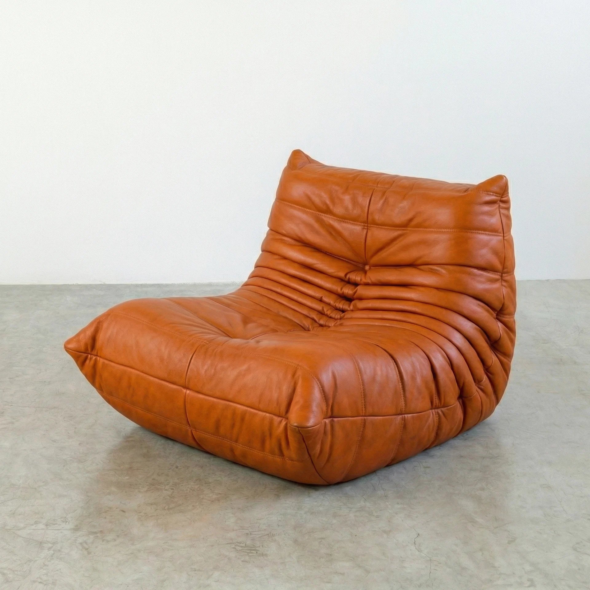 Togo Chair Dupe in cognac real cowhide leather on a concrete floor with a white wall background