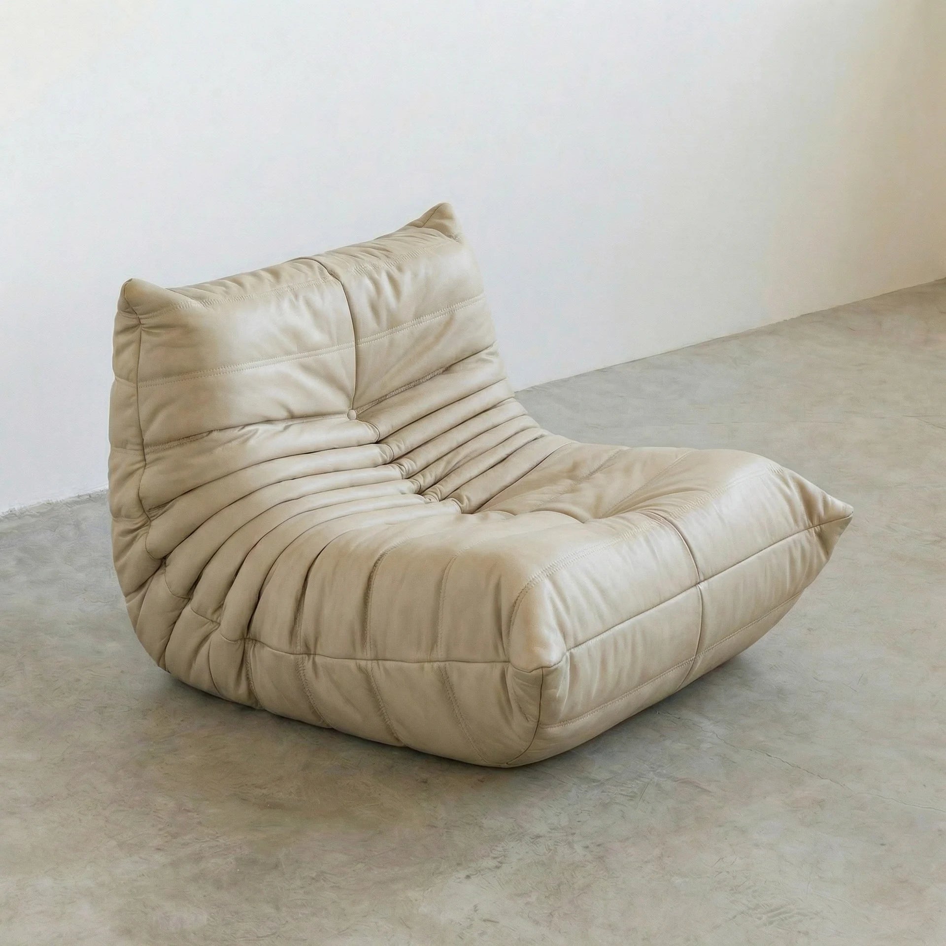 Togo Chair Dupe in cream real cowhide leather on a concrete floor with a white wall background
