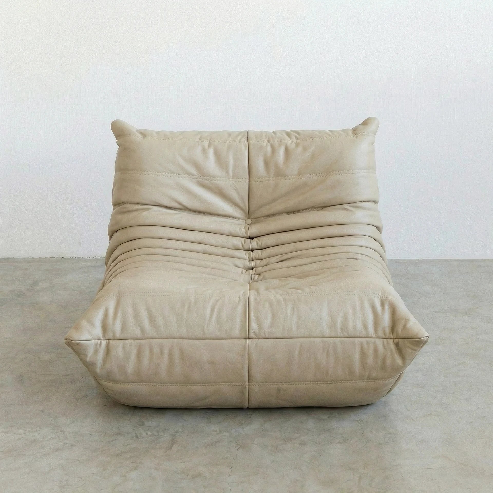 Togo Chair Dupe in cream real cowhide leather on a concrete floor with a white wall background