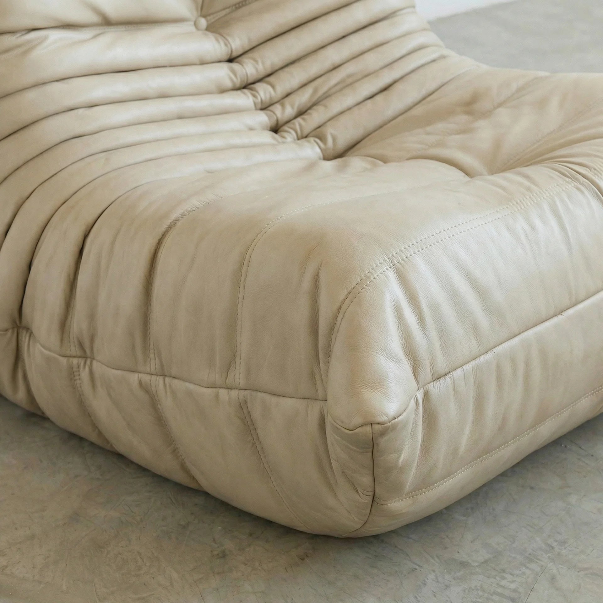 close-up of the Togo Chair Dupe in cream real cowhide leather on a concrete floor with a white wall background