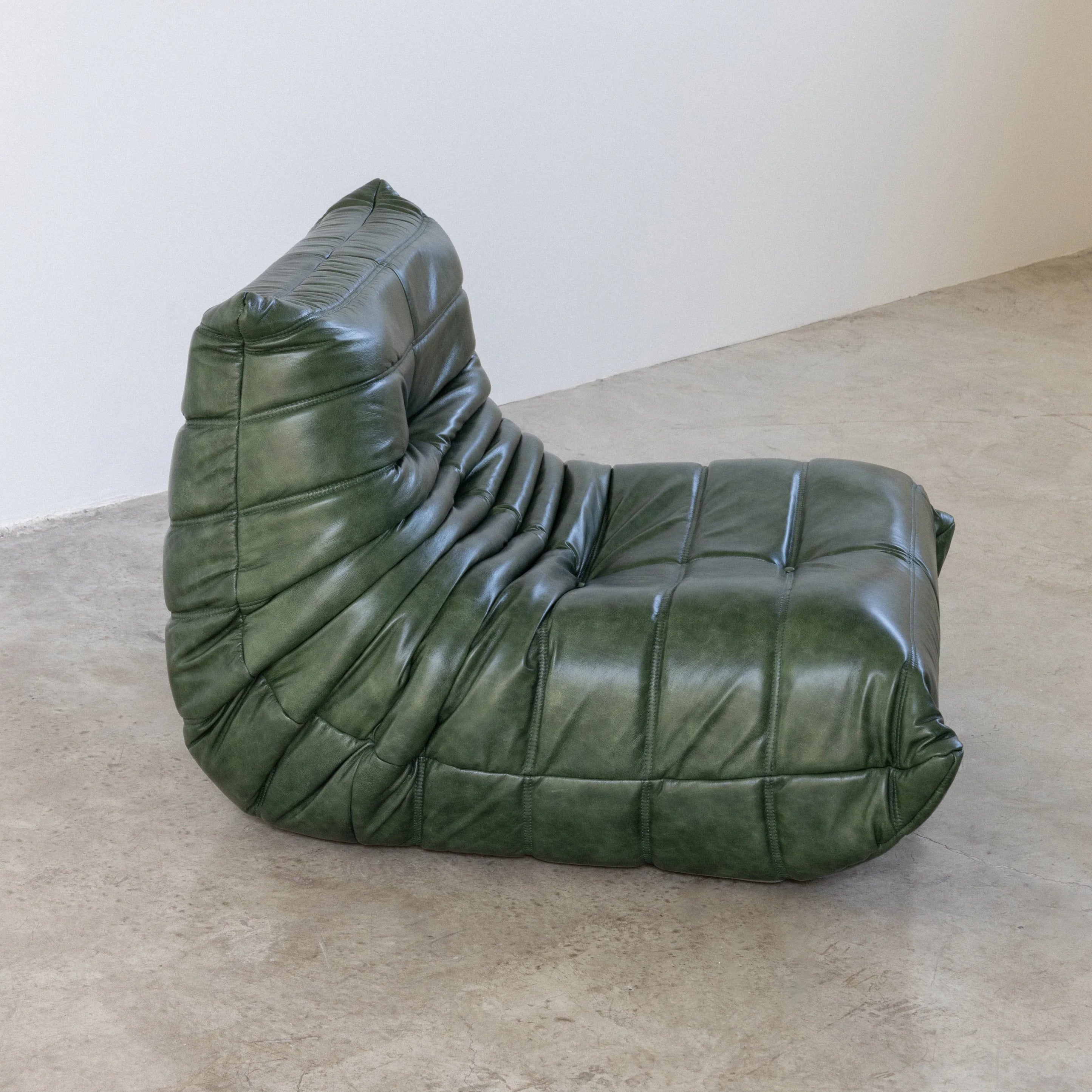 Togo Chair Dupe in green real shiny oil wax leather on a concrete floor with a white wall background