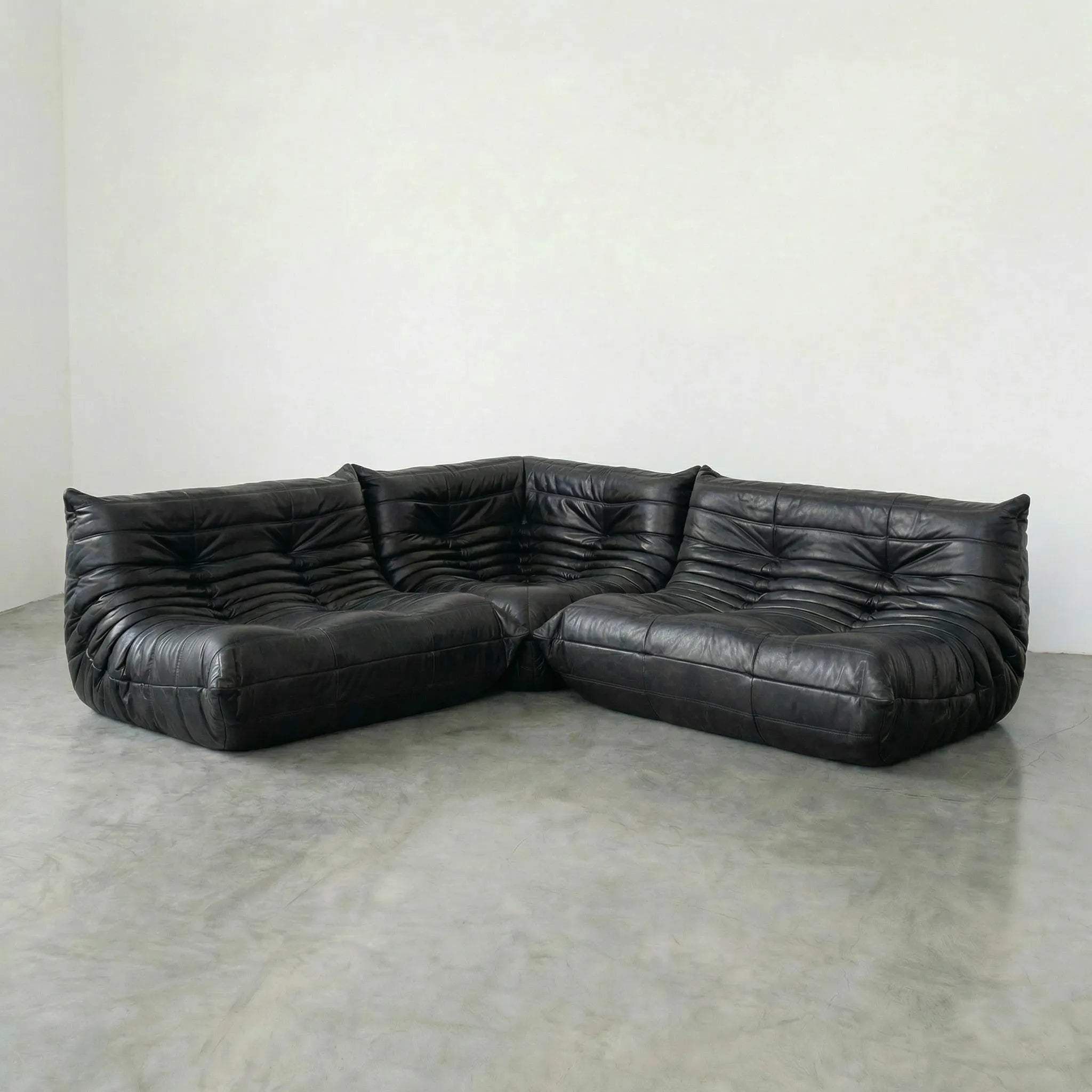 Black leather sectional togo sofa dupes on a concrete floor with a white wall background