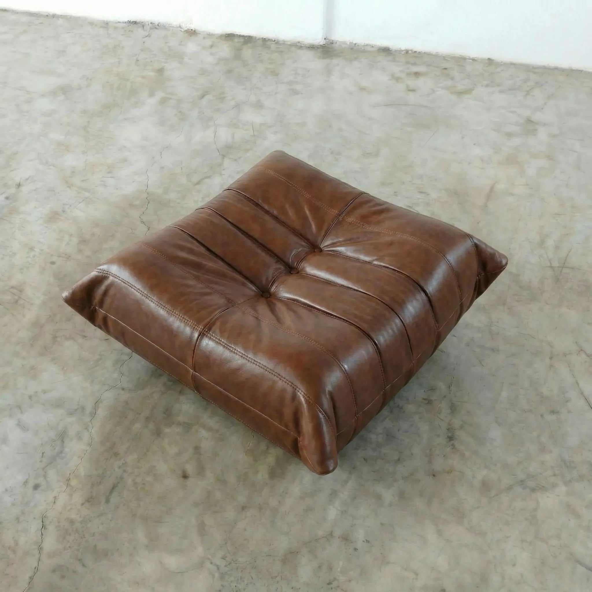 Brown togo leather ottoman dupe on a textured floor