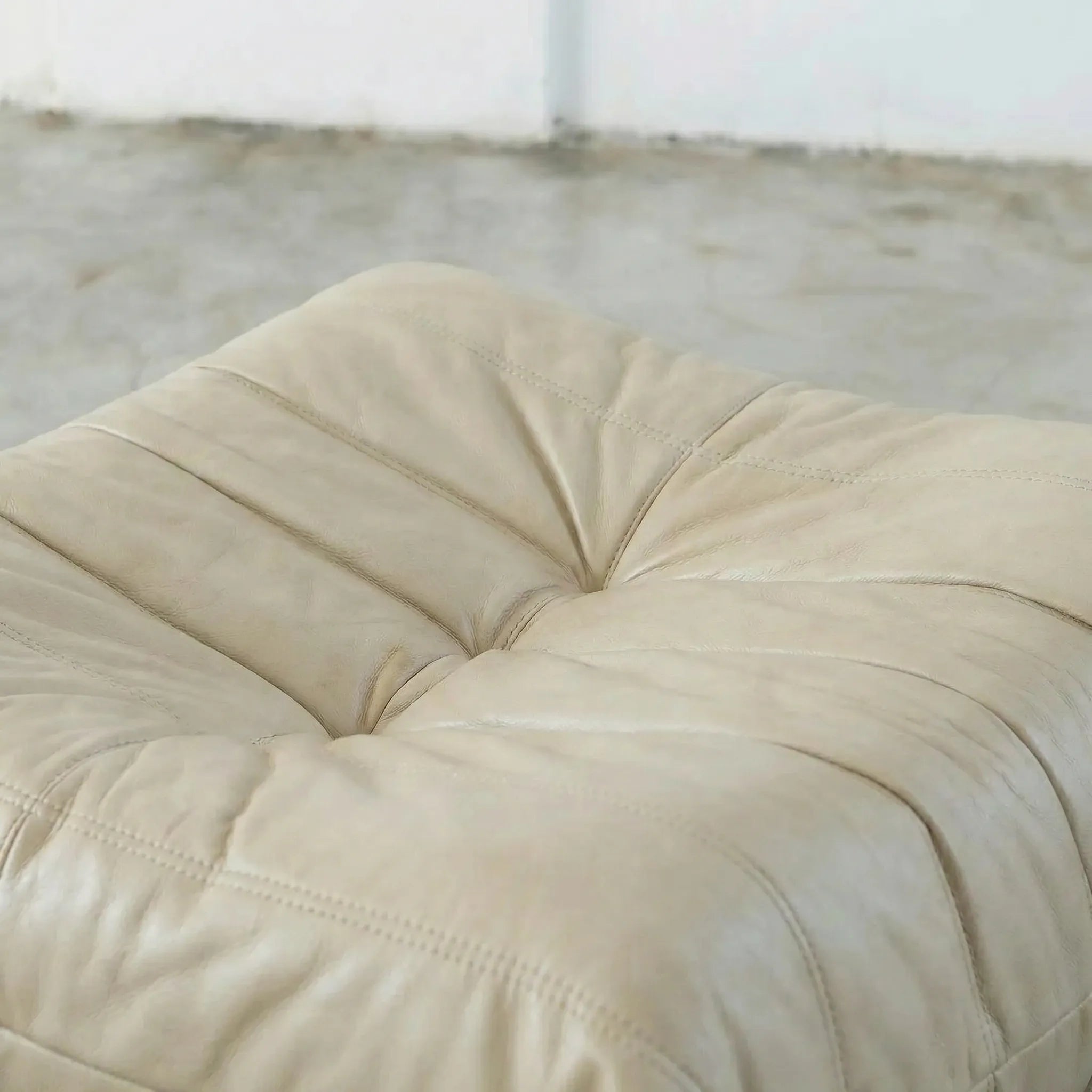 Beige togo leather ottoman dupe on a concrete floor with white walls