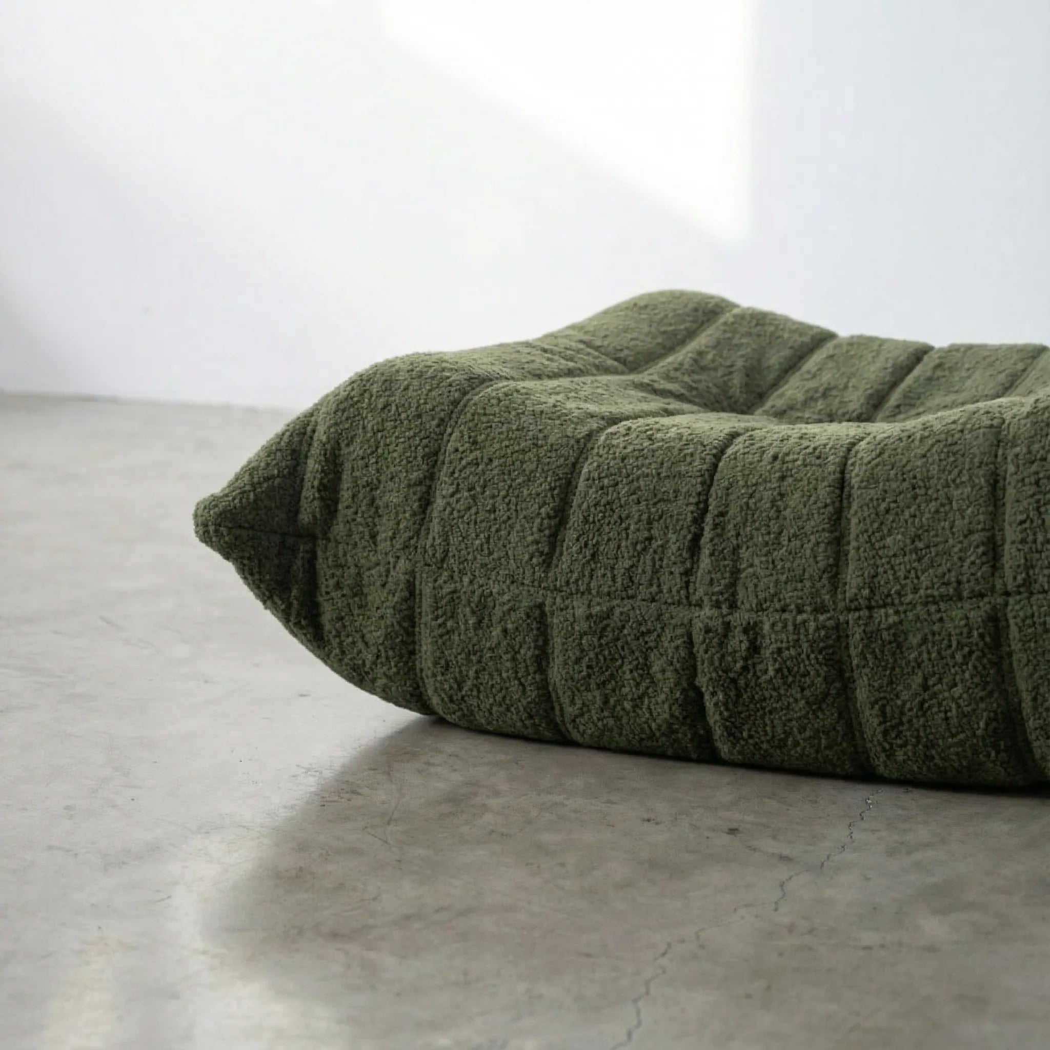 Close-up of dark green togo ottoman replica in bouclé on a concrete floor.