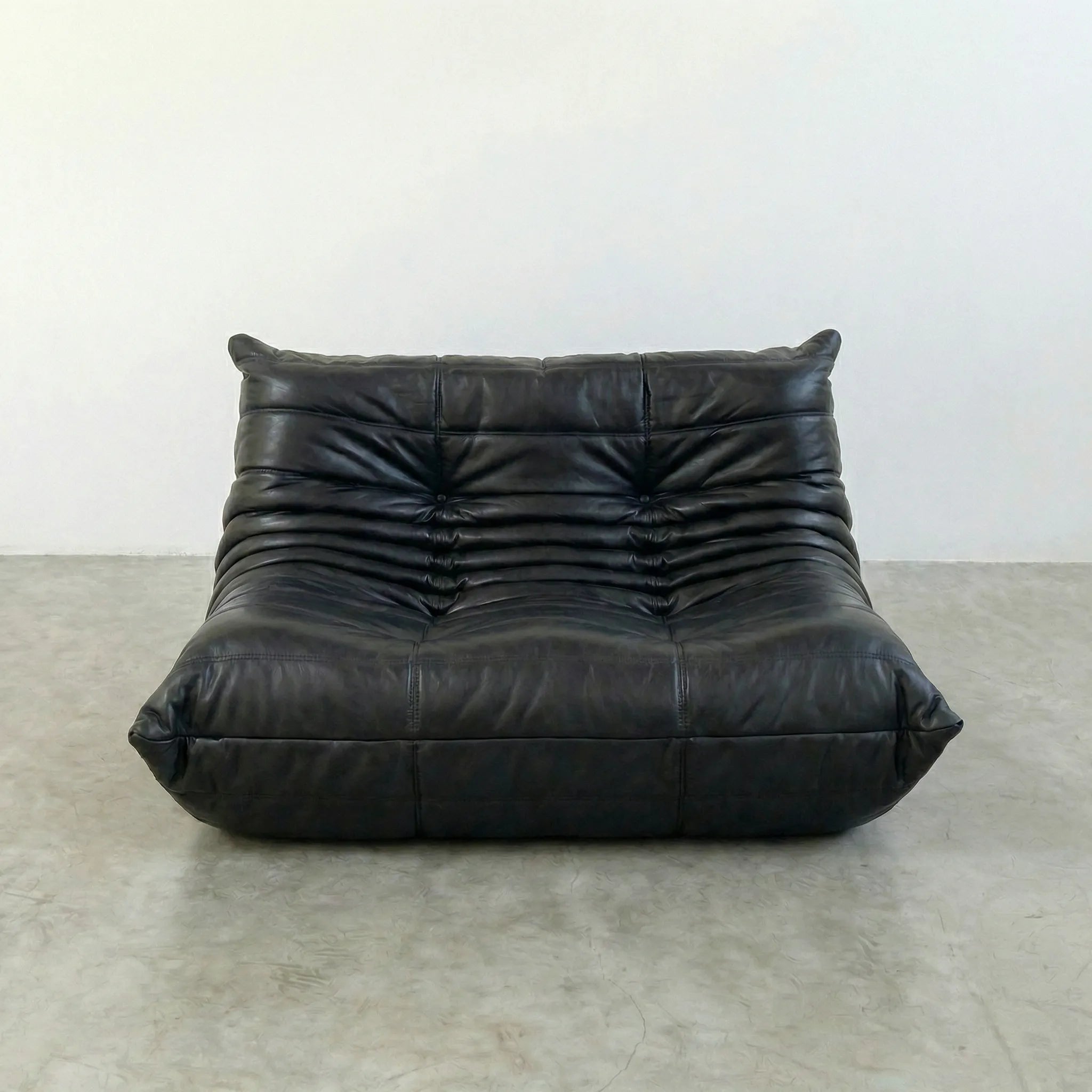 togo sofa dupe in black leather on a concrete floor with a white wall background