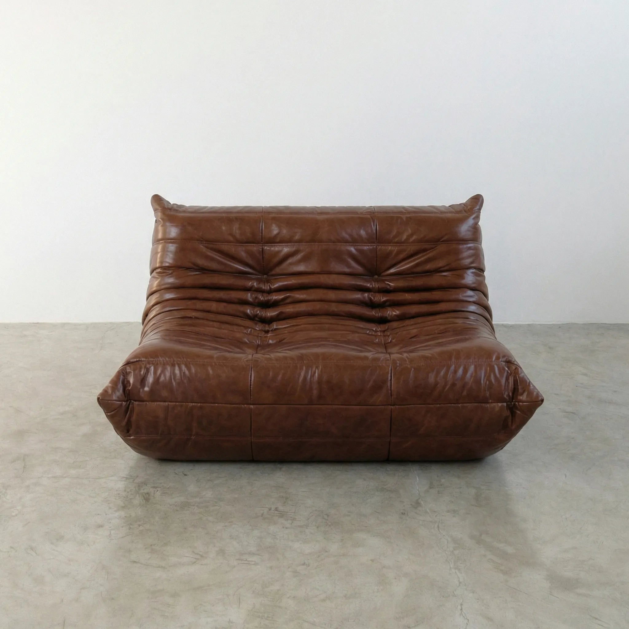Brown togo sofa in leather on a concrete floor with a white wall background