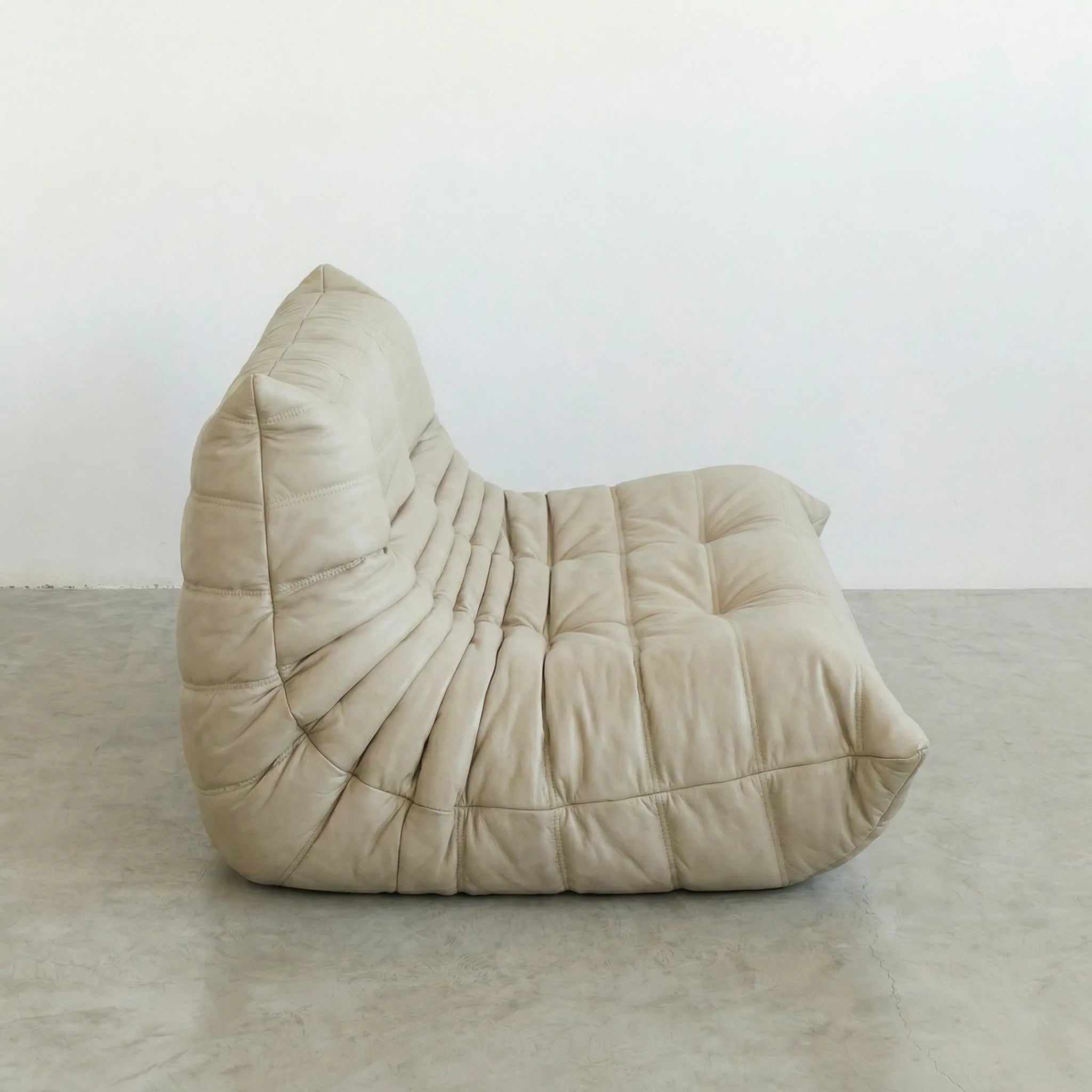 Beige togo sofa dupe on a concrete floor with a white wall background