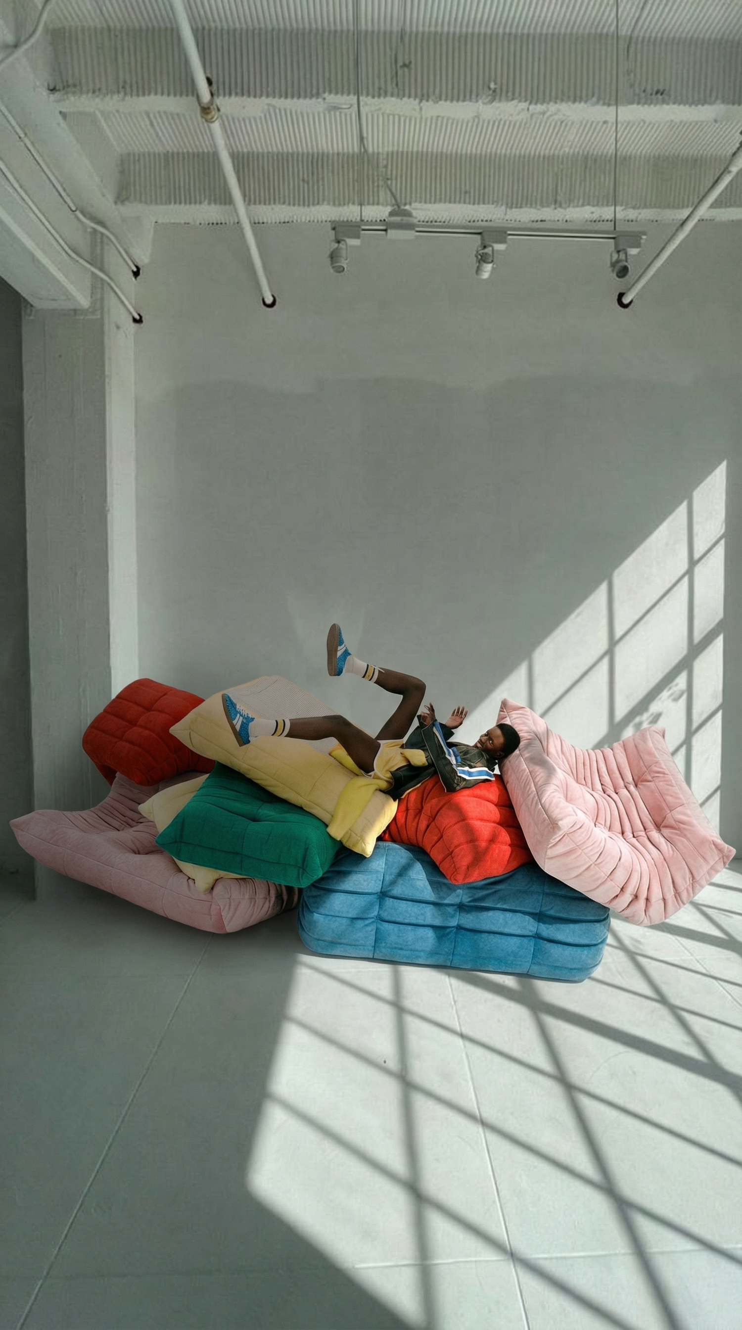 Person lying on colorful togo chairs in a room with large windows by vibehaus