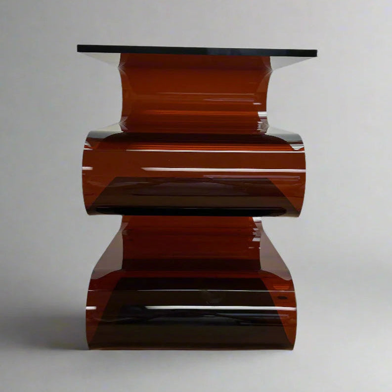 Modern acrylic s-shaped side table with a glossy amber red base and clear glass top on a gray background