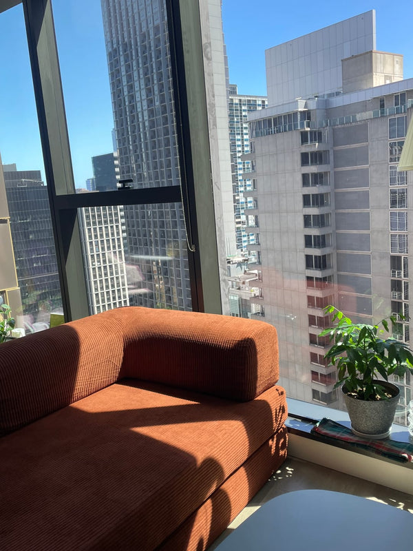 Orange sofa in a room with large windows overlooking city buildings