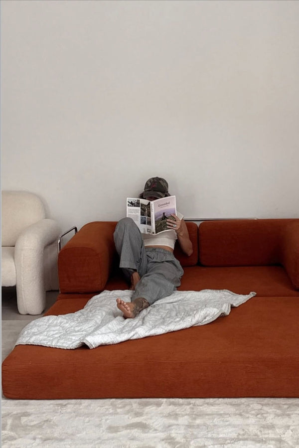 Person reading a book on a brown sofa with a white blanket