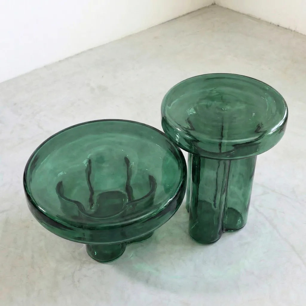 Two green round glass side tables on a concrete  floor.