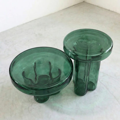 Two green round glass side tables on a concrete  floor.