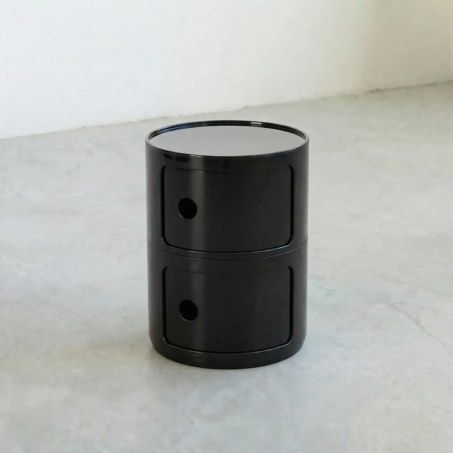 Black glossy round modular storage unit, Kartell Componibili dupe with two tiers in minimalist concrete studio