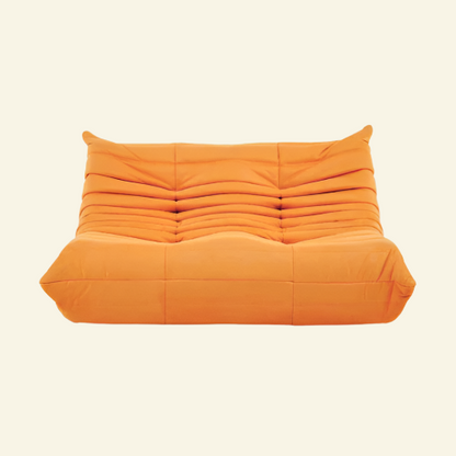 Togo-style orange 2-seater velvet sofa with low-profile design, plush channel tufting, and sculptural curves — inspired by Michel Ducaroy, ideal for modern interiors.