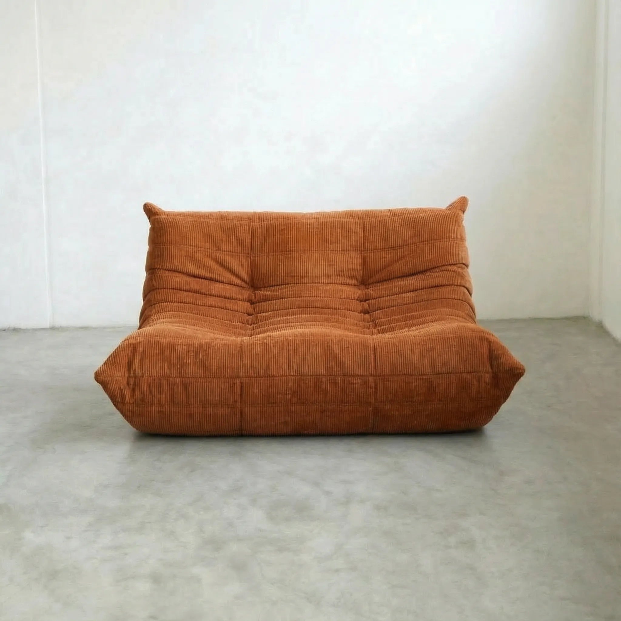 Togo 2 Seater Sofa Dupe in orange corduroy, inspired by michael ducaroy, on concrete floor