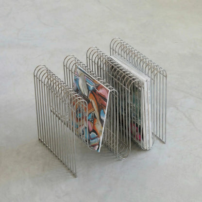 Vintage chrome curved magazine rack holding books and vinyl records on a concrete floor.