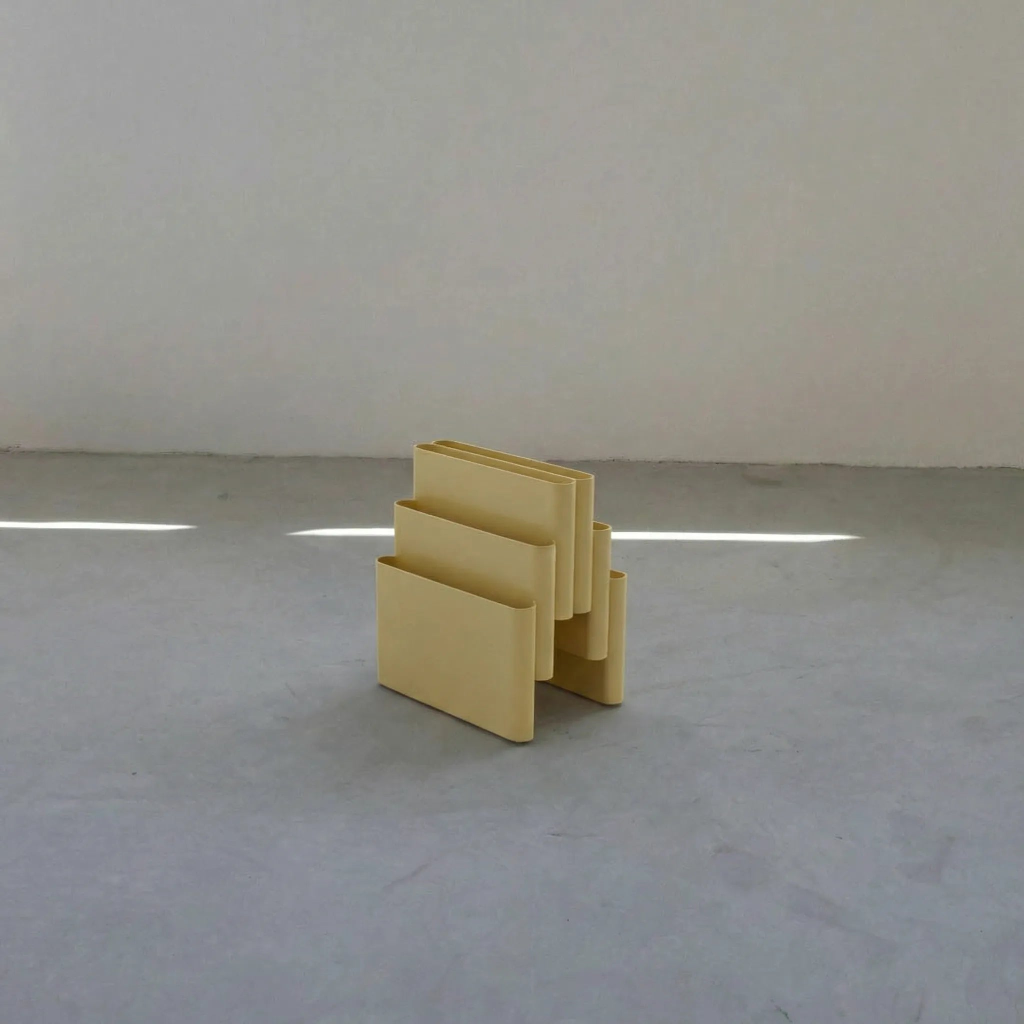 Yellow Kartell magazine rack replica on a white surface