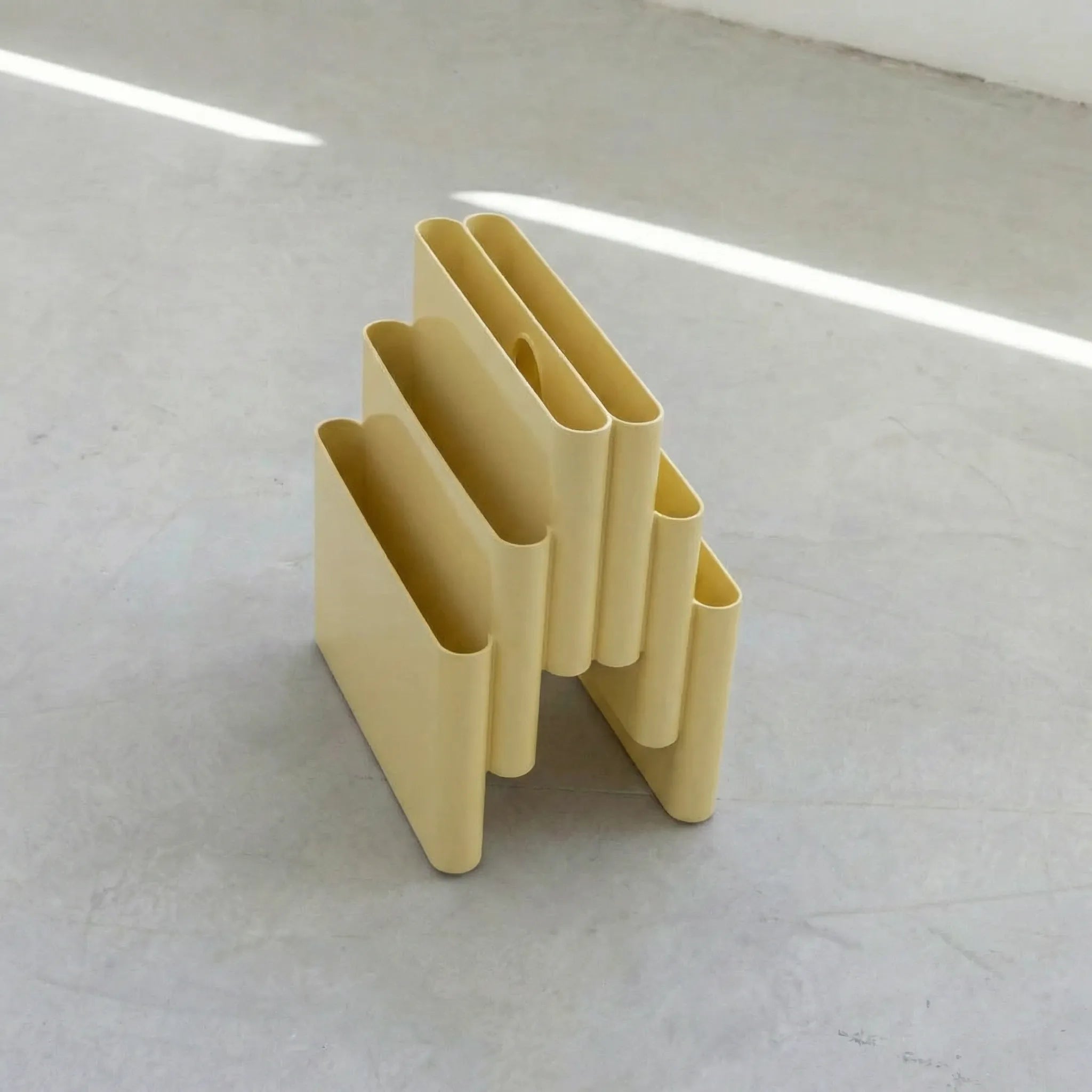 Yellow Kartell magazine rack replica on a white surface