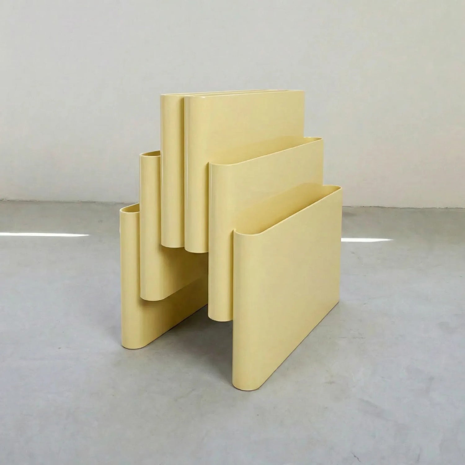 Yellow Kartell magazine rack replica on a white surface