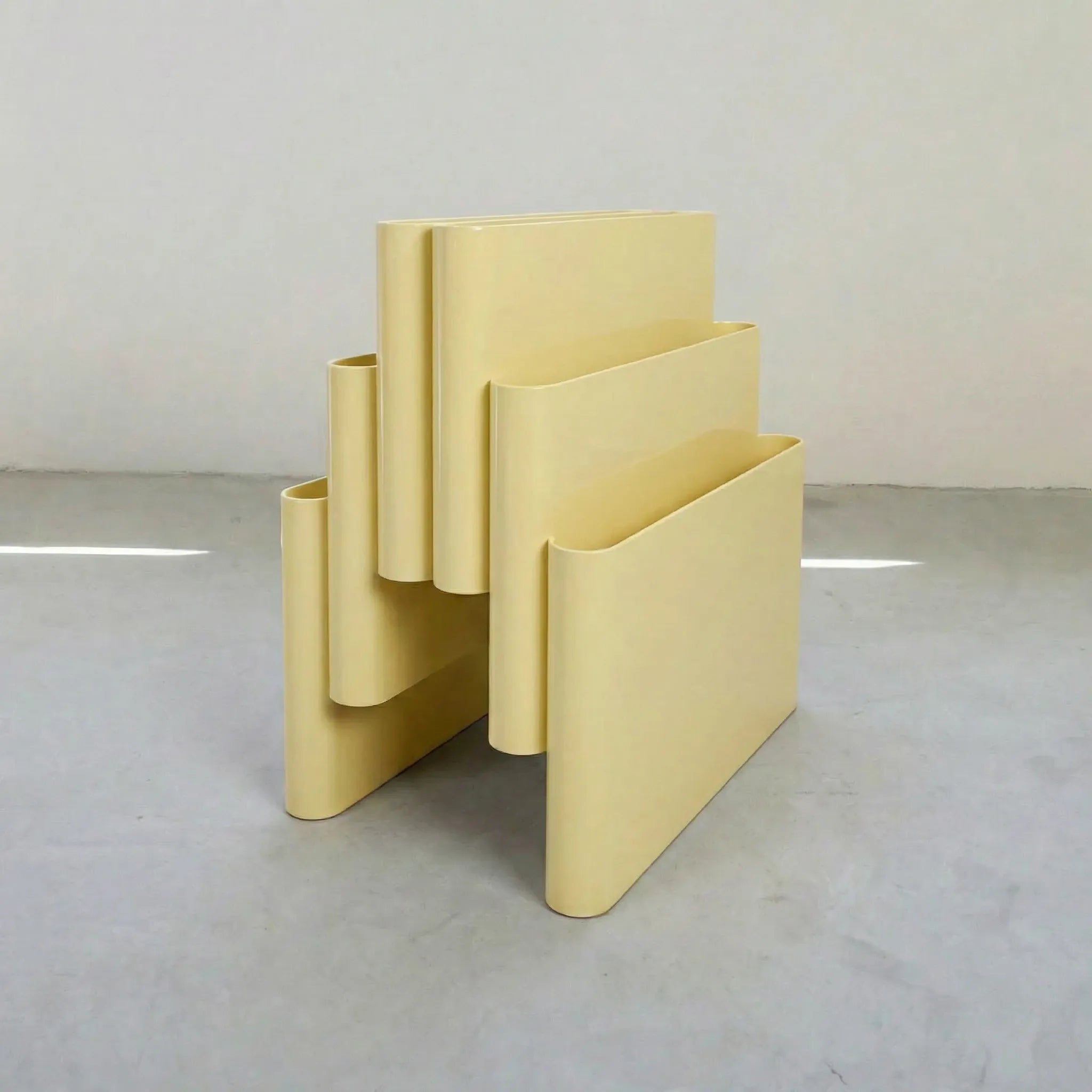 Yellow Kartell magazine rack replica on a white surface