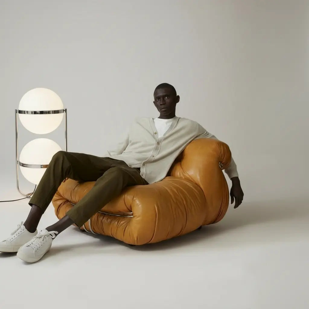 Person sitting on a brown leather chair with the Zuru globe floor lamp dupe next to him.