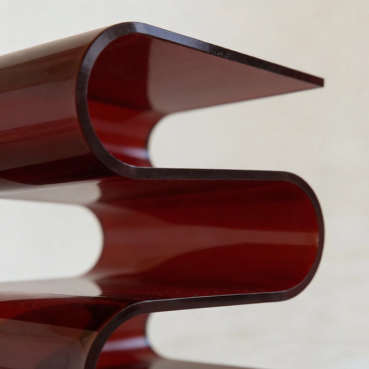 Close up of the acrylic s-shaped side table with a glossy amber red base and clear glass top on a gray background