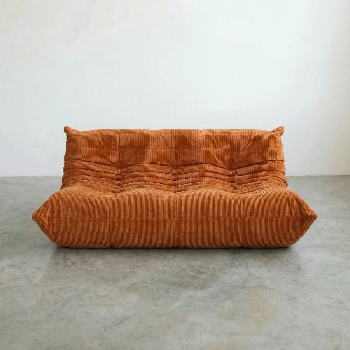 Bruma 3 seater sofa in orange corduroy on a concrete floor, photographed from a front angle.