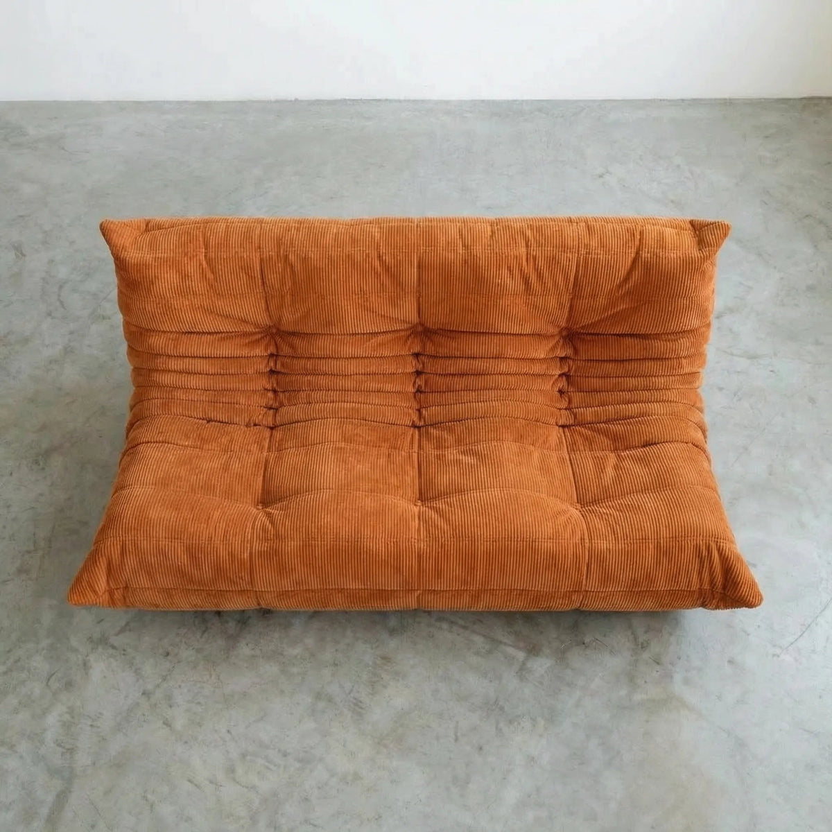 Bruma 3 seater sofa in orange corduroy on a concrete floor, photographed from a top angle.