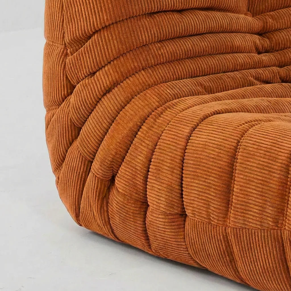 Close up of a corner of the Bruma 3 seater sofa in orange corduroy on a concrete floor.