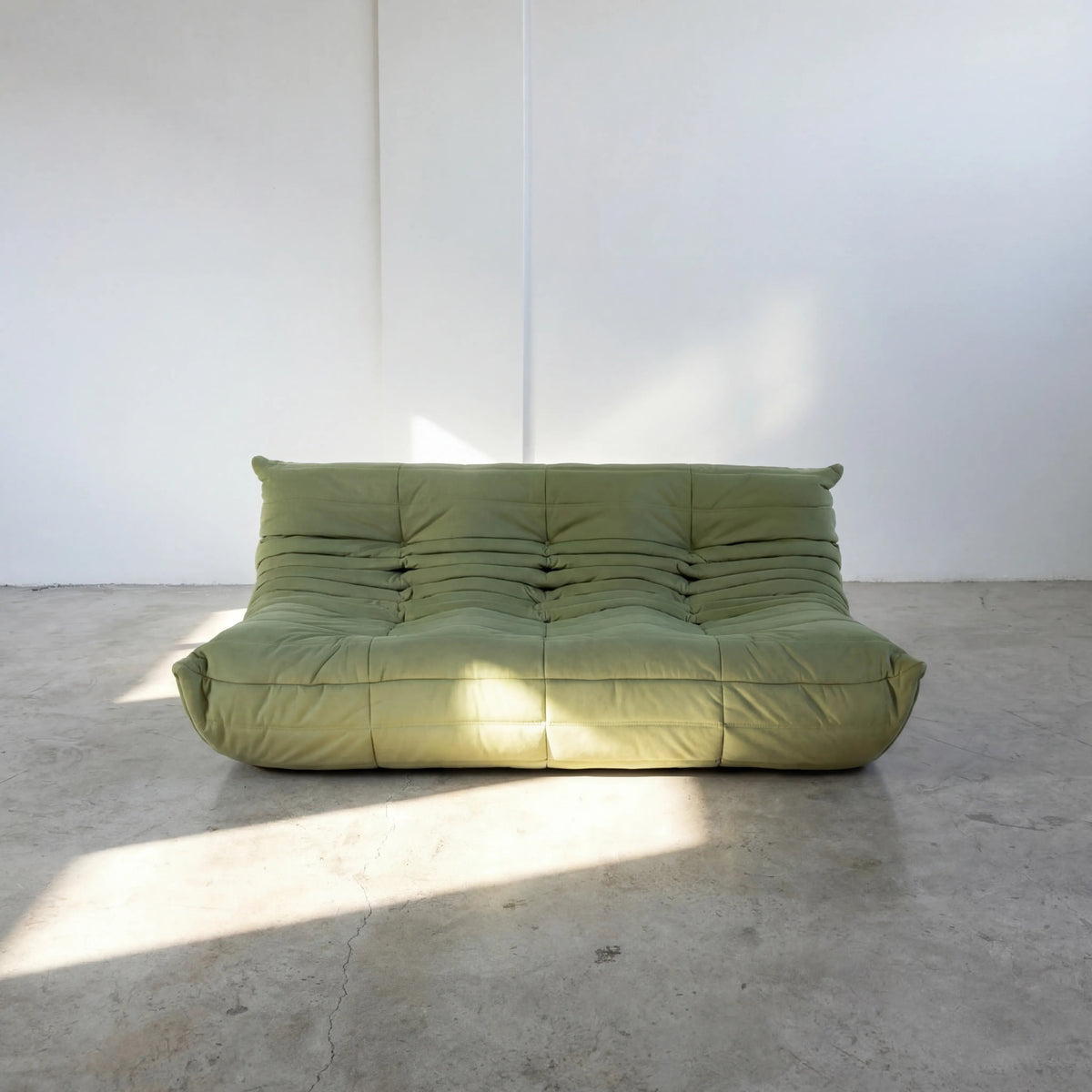 Bruma 3 seater sofa in Green Velvet Suede by vibehaus on a concrete floor, photographed from a front angle.